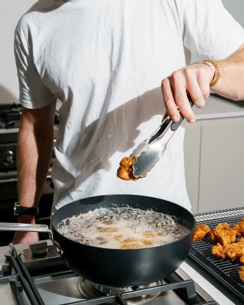 Tongs lifting golden fried chicken out of a black frying pan