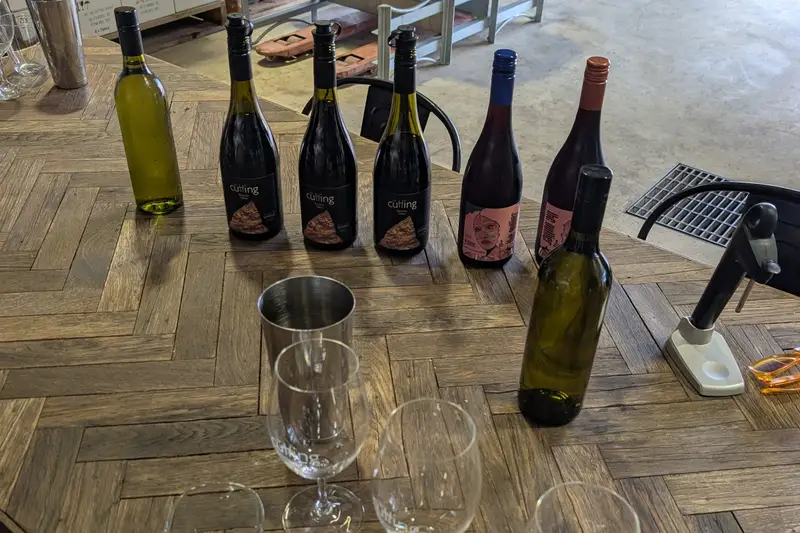 Wine bottles and tasting glasses on a wooden table beside barrels