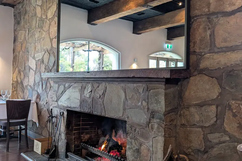 Stone fireplace burning in a timber-beamed dining room