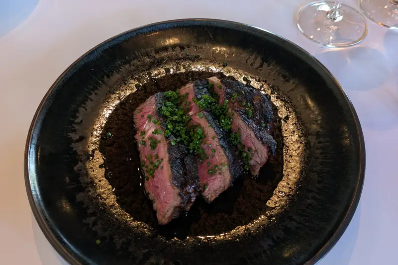 Sliced steak on a black plate with wine glasses