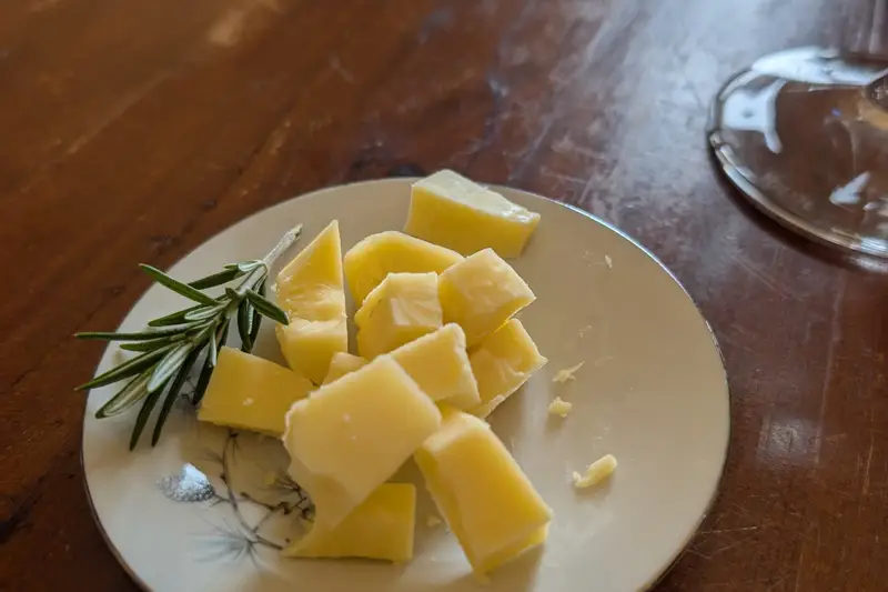 Plate of cheese cubes with a rosemary sprig on a timber table