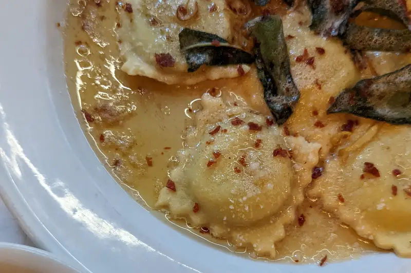 Ravioli in a buttery sauce beside a dish of olive oil
