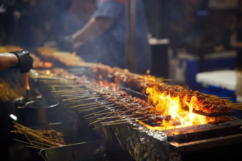 Satay skewers cooking over flaming charcoal