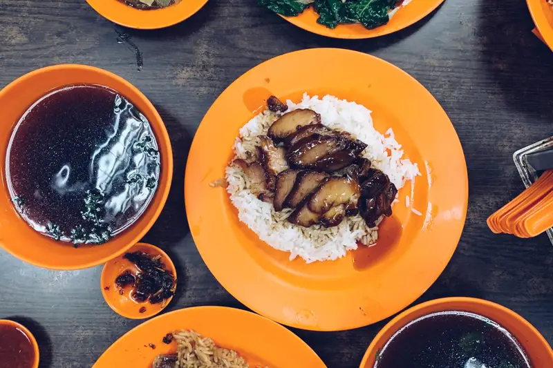 Spread of hawker dishes in orange bowls on a dark table