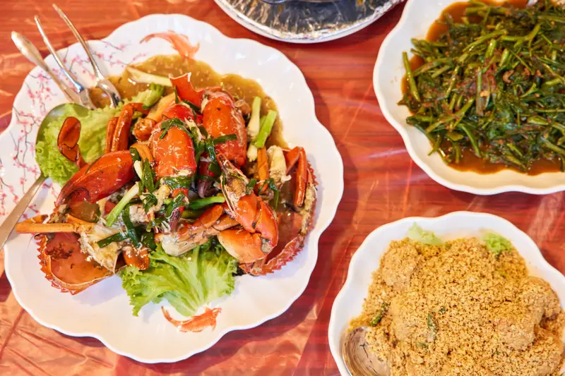 Crab in red sauce with greens and fried noodles on patterned plates