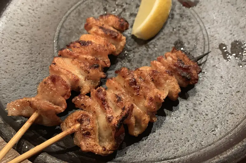 Chicken yakitori skewers with a lemon wedge on a dark stone plate