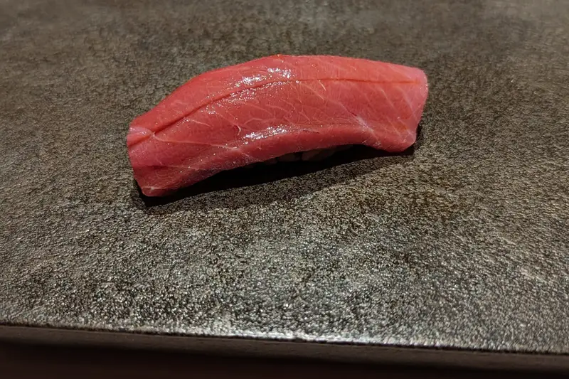 Single piece of tuna nigiri on a dark stone plate at a sushi counter