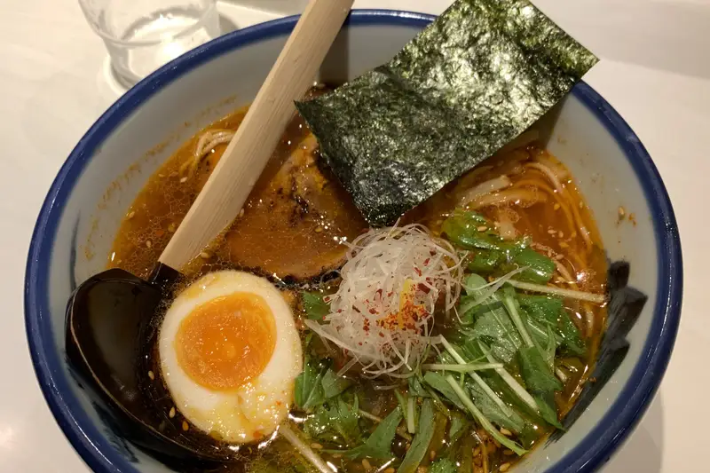 Bowl of spicy ramen with a soft egg, nori and greens