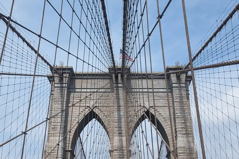 The Brooklyn Bridge walkway, looking up at the stone tower and cables