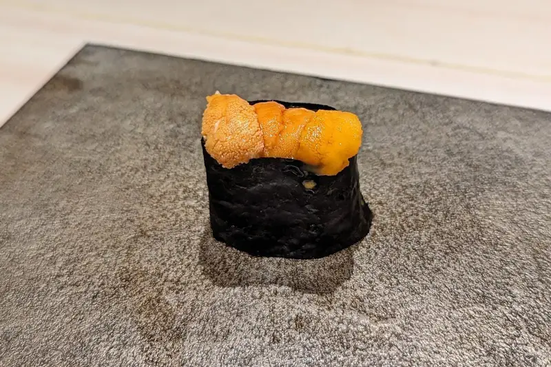 A piece of uni nigiri on a stone plate at a Tokyo sushi counter
